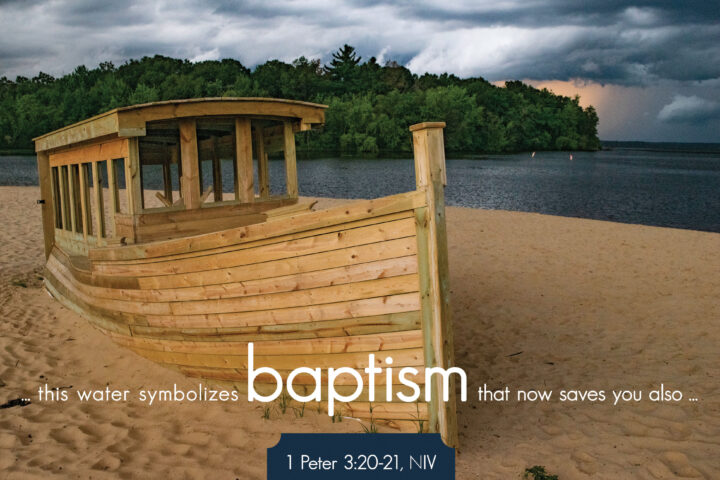 Weathered wooden boat on a sandy beach with a forested lake in the background and dark storm clouds above.