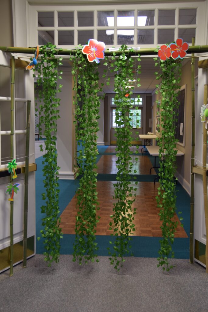 Indoor hallway decorated with hanging green ivy on bamboo arches and large red hibiscus flowers on the sides.